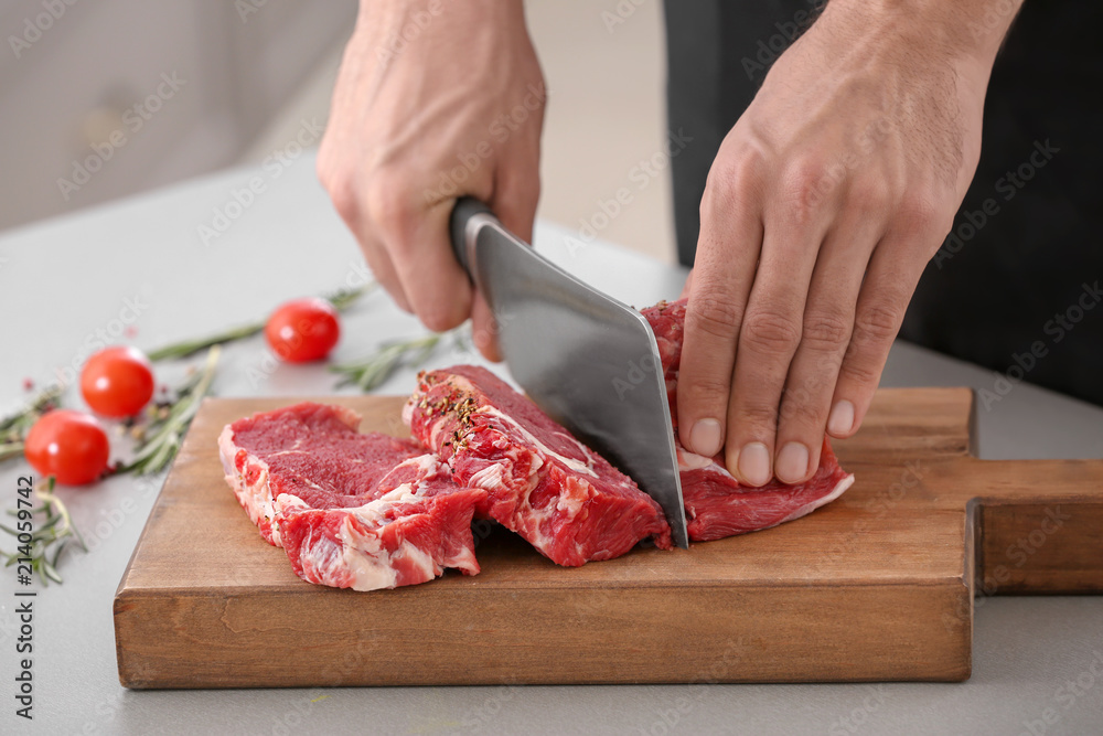 Man cutting fresh raw meat on wooden board in kitchen