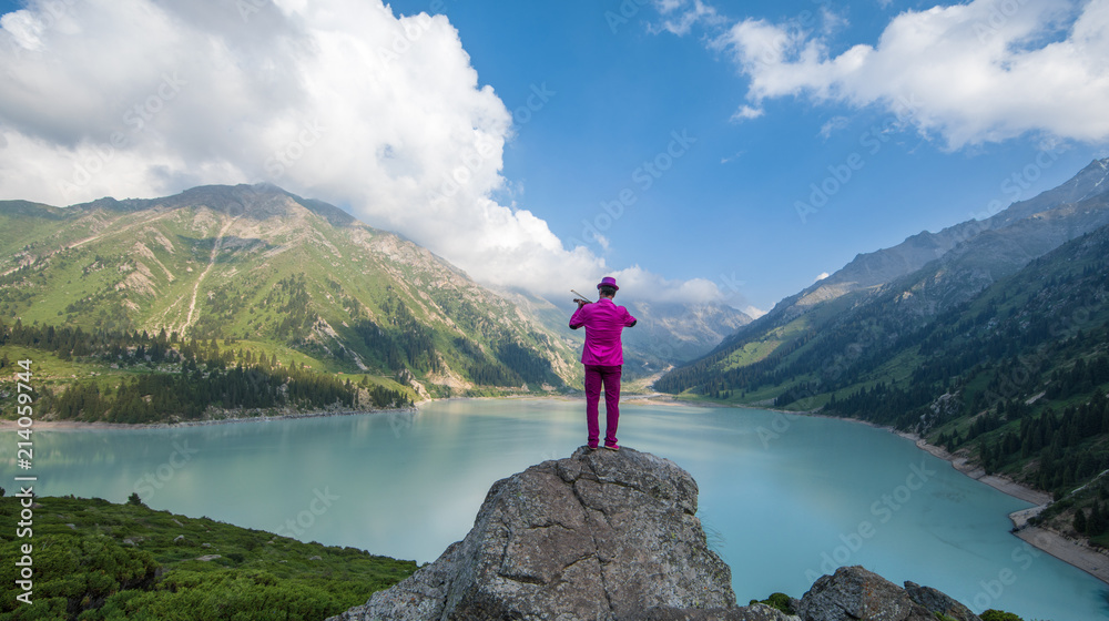 violinist in a red suit playing the violin on the background of a mountain lake