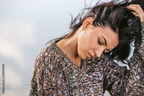 Closeup portrait of beautiful dreamy brunette female with closed eyes posing against lake with blowing hair. People, lifestyle and travel concept. Sensual natural female posing in sweater