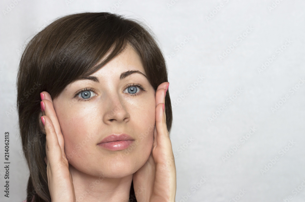 A young attractive woman looks at her face. Clean skin. The first signs of aging. Care for youth. A young attractive woman looks at her face. Clean skin. The first signs of aging. Care for youth.