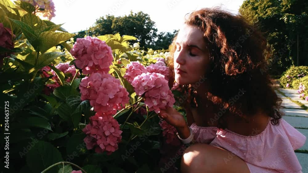 Young pretty woman smelling flowers in the garden
