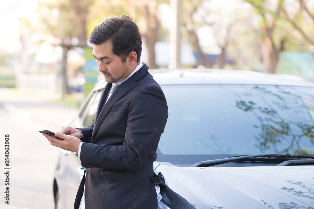 Handsome businessman using a mobile phone lerning on his car