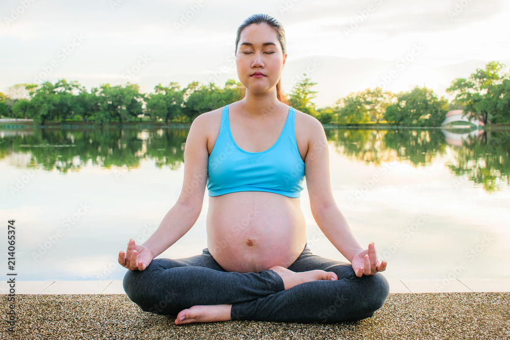 Pregnancy exercise. Prenatal yoga. Pregnant woman doing yoga beside the lake. Relaxing moment.
