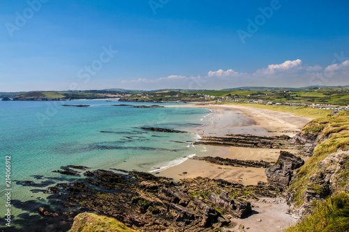 Amazing coastal landscape. Beach, crystal clear water, stones, rocks, cliffs. Typical view from Ireland. Very popular travel holiday destination. Idyllic day by ocean, blue skies, few clouds.