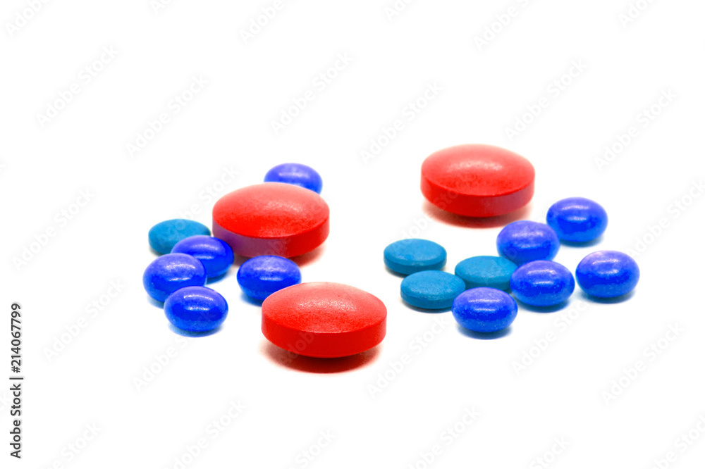 Red tablets and colored pills scattered on the table. A concept with an emphasis on red pills. Isolated on white background. For design in pharmacology, pharmacy, dietary supplements, drugs. Red tablets and colored pills scattered on the table. A concept with an emphasis on red pills. Isolated on white background. For design in pharmacology, pharmacy, dietary supplements, drugs.