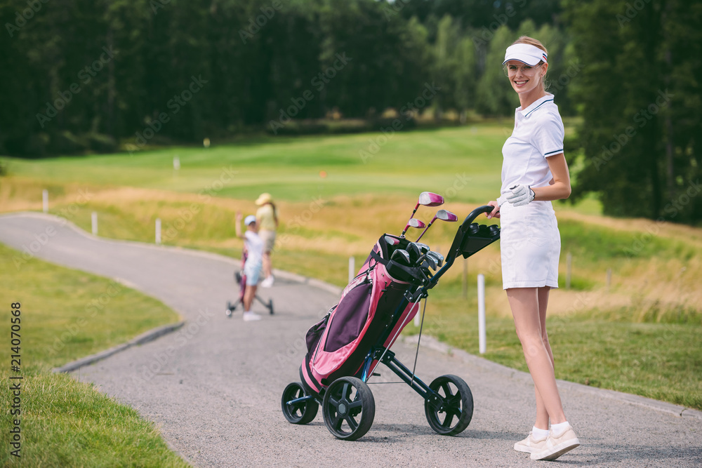 selective focus of smiling female golf player in cap and white polo with golf gear at golf course selective focus of smiling female golf player in cap and white polo with golf gear at golf course