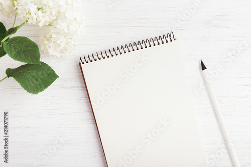 Working place with notebook, pencil and flower on white wooden table. Planning concept, top view.