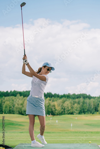 Side view of woman in polo, sunglasses and cap playing golf at golf course
