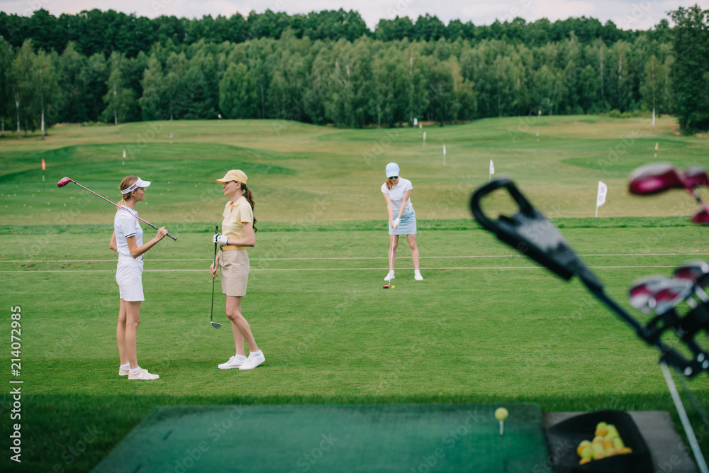 selective focus of women in caps with golf equipment at golf course