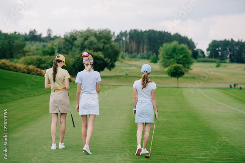 rear view of women in caps with golf equipment walking at golf course