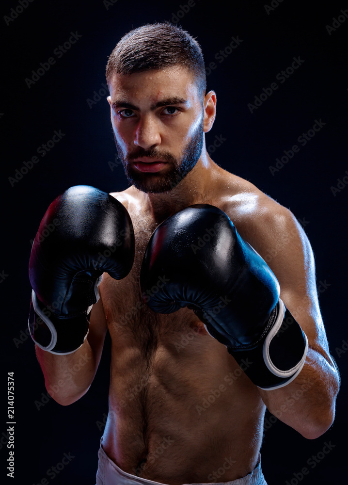Strong muscular boxer in black boxing gloves. A man in a boxing stand on black background.