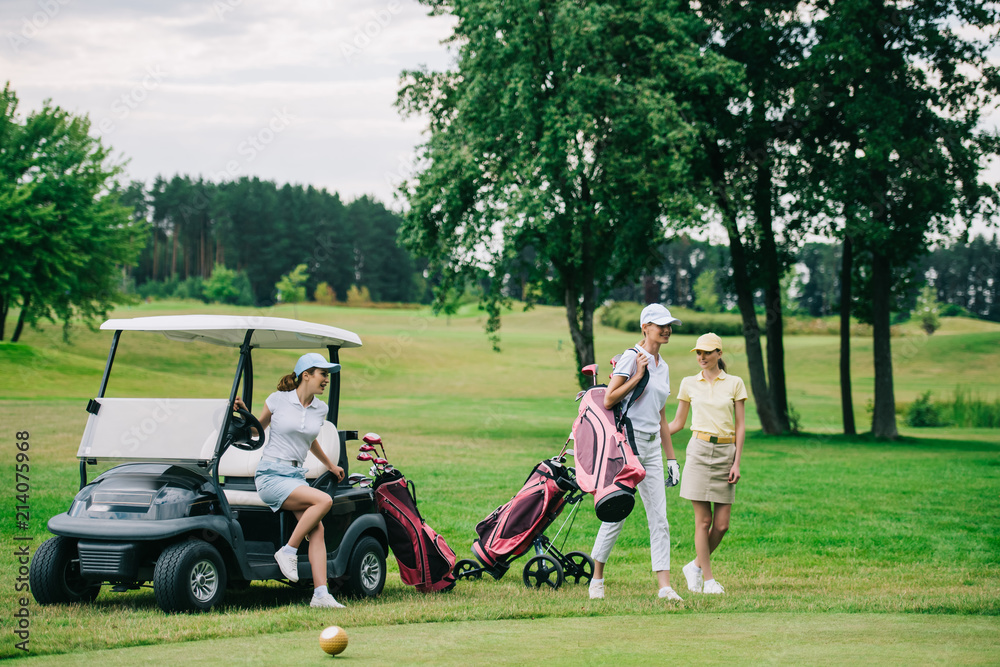 group of female golf players in caps with golf equipment at golf course on summer day group of female golf players in caps with golf equipment at golf course on summer day