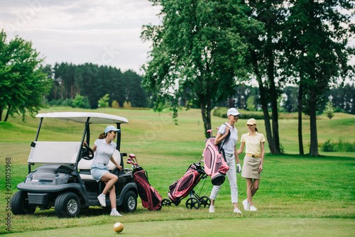 group of female golf players in caps with golf equipment at golf course on summer day