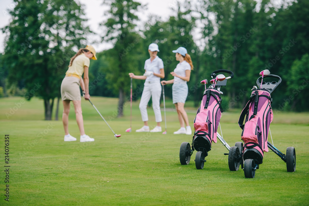 selective focus of golf gear, woman in cap with golf club and friends standing near by at golf course selective focus of golf gear, woman in cap with golf club and friends standing near by at golf course