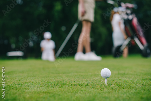 Selective focus of golf ball on green lawn and golf players behind