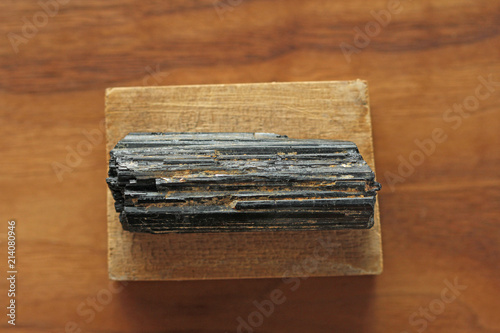 Black tourmaline stone on a background of natural wood American black walnut. Mineral collection stones. Stone is a sherl tourmaline. Black Crystal photo