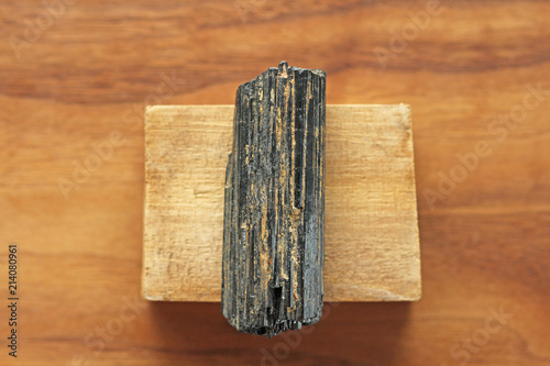 Black tourmaline stone on a background of natural wood American black walnut. Mineral collection stones. Stone is a sherl tourmaline. Black Crystal photo
