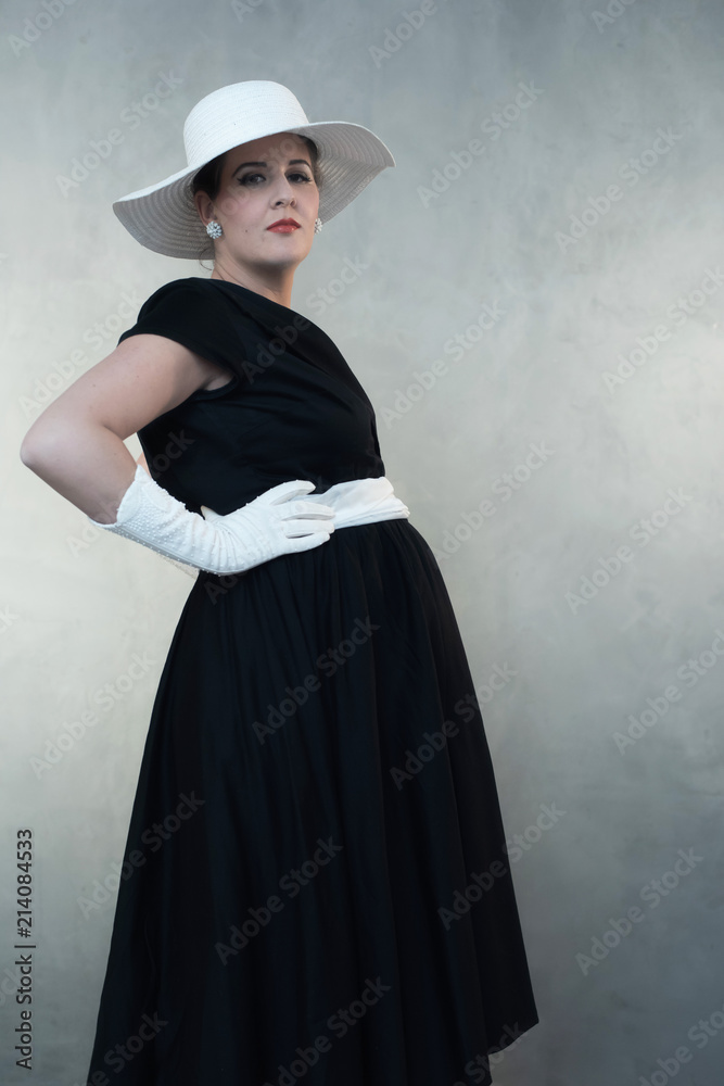 Retro 1950s pregnant woman in white hat and black dress. Looking towards camera. Retro 1950s pregnant woman in white hat and black dress. Looking towards camera.