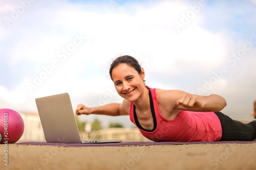 fit woman watching online fitness program and doing workout infront of a laptop on a mat photo