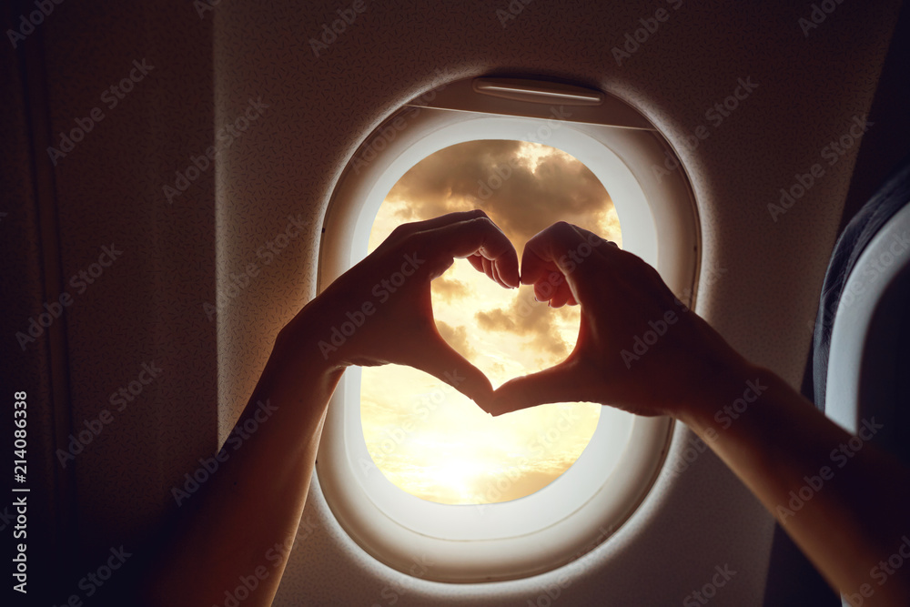 Obraz premium The concept of travel. Hands in the shape of heart on the background of the airplane window. 