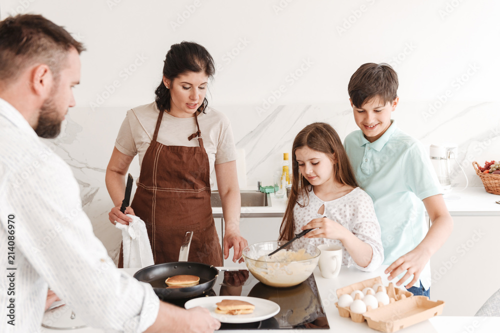 Lovely big family mother and father with two kids 8-10 cooking together, and frying pancakes on modern stove in kitchen at home Lovely big family mother and father with two kids 8-10 cooking together, and frying pancakes on modern stove in kitchen at home