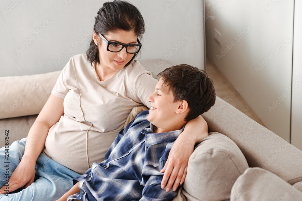 Photo of happy family mother and son resting in living room in apartment, and sitting on sofa together Photo of happy family mother and son resting in living room in apartment, and sitting on sofa together