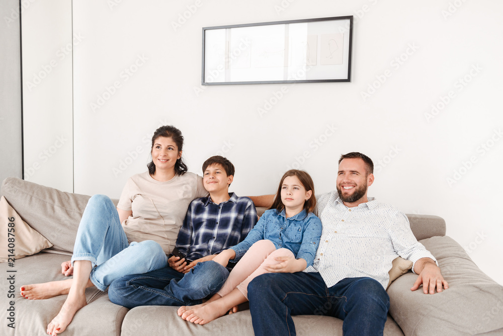 Image of caucasian family with two children resting in living room at home, and looking at tv together while sitting on sofa