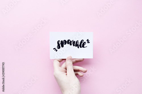 Fotografiet Minimal composition on a pink pastel background with girl's hand holding card wi