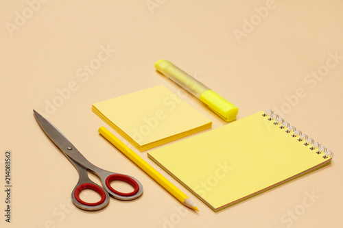 Scissors, pencil, notebook, note-paper and yellow felt-tip pen on beige background