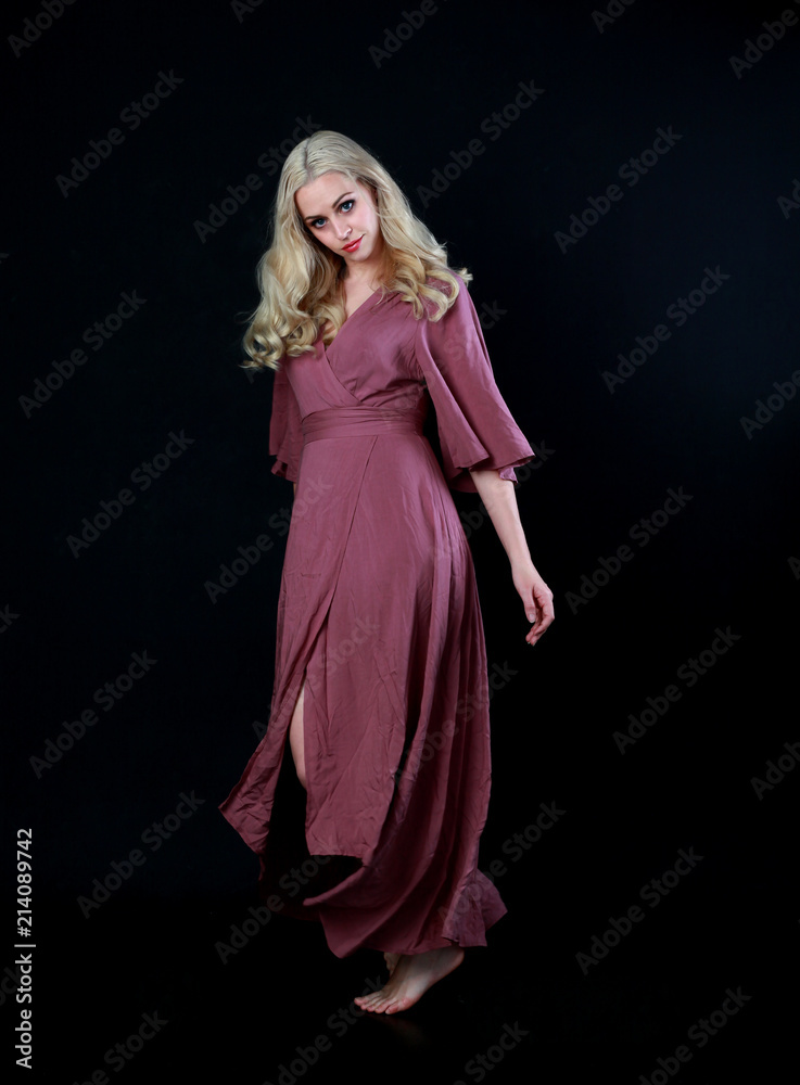 full length portrait of blonde girl wearing long purple dress. standing pose. black studio background. full length portrait of blonde girl wearing long purple dress. standing pose. black studio background.