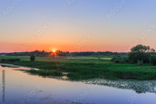 Landscape with sunset over meadows on the river shore