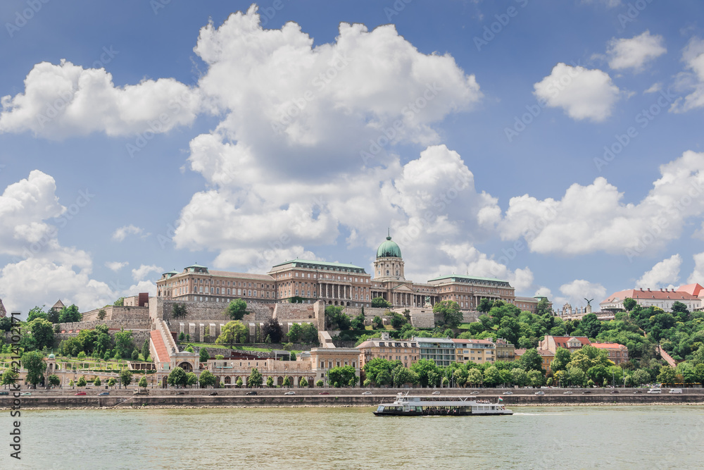 Budapest cityscape with a touristic ship  sailing on the Danube river under the dramatic cloudy sky. Historic Buda Castle on the hill towering over the water.
