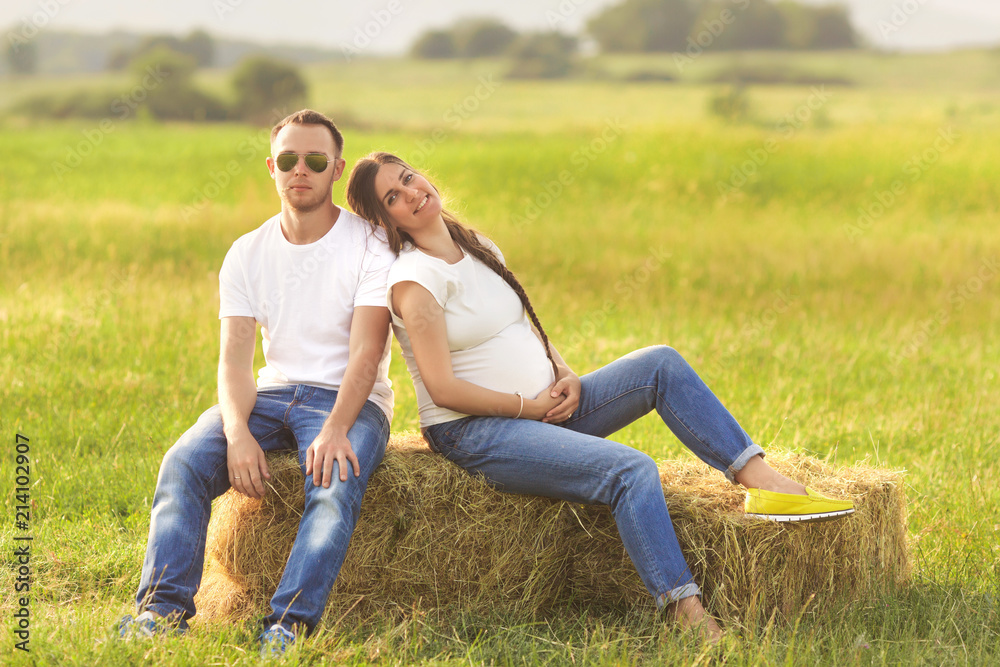 Young pregnant woman with her husband enjoying the nature wearing casual and style jeans and white t-shirt. Young pregnant woman with her husband enjoying the nature wearing casual and style jeans and white t-shirt.