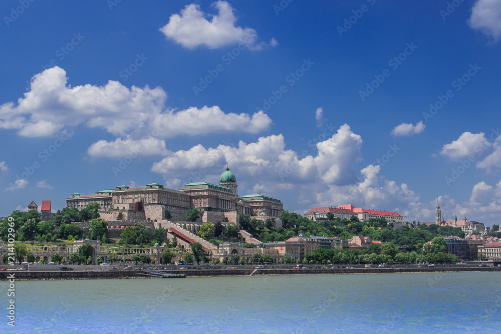 Budapest cityscape with the Buda Castle building and Castle Bazaar Gardens towering over the Danube under the blue cloudy sky. Boat sailing on the river.