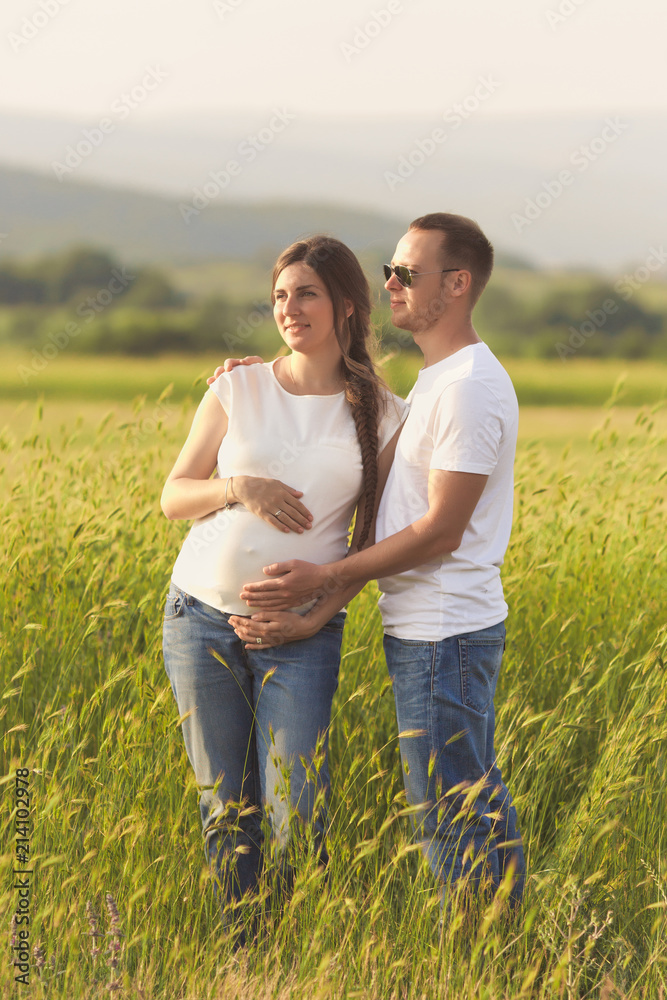 Young pregnant woman with her husband enjoying the nature wearing casual and style jeans and white t-shirt. Young pregnant woman with her husband enjoying the nature wearing casual and style jeans and white t-shirt.