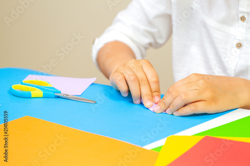 Kid hands making greeting card with colored paper at the table