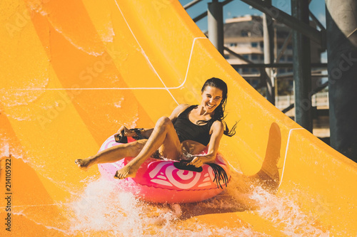 pretty smiling woman on the rubber ring having fun on the orange water slide in the aqua park. Summer Vacation. Weekend on resort