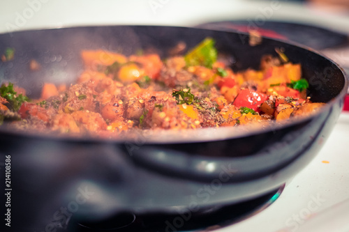 A pan of pasta sauce including peppers, sausage, carrots, kale, and assorted spices.