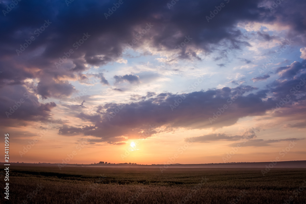 Sunrise or sunset over the field in the summer. Dark dramatic clouds over the field in the morning during the sunrise_