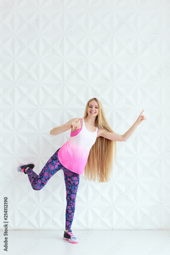 Smiling sporty woman wearing sportswear with hands rised up over white wall