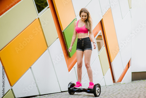 Young beautiful woman dressed in shorts and t-shirt with hoverboard on colored wall background