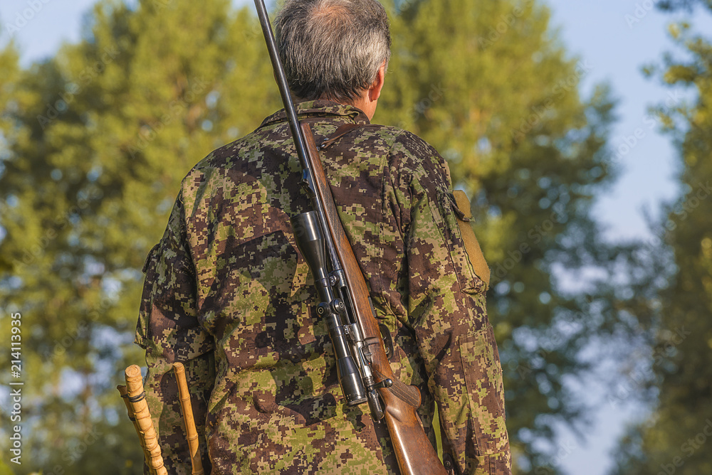 One hunter in camouflage clothing with carbine with optical sight back view close up on sunny day