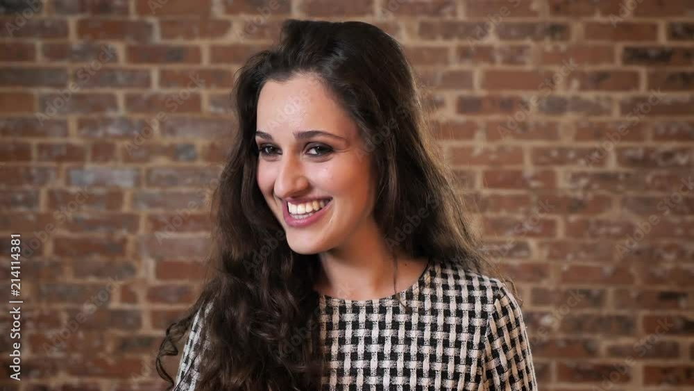 Beautiful woman with dark curly hair is smiling, jumping, brick background Beautiful woman with dark curly hair is smiling, jumping, brick background