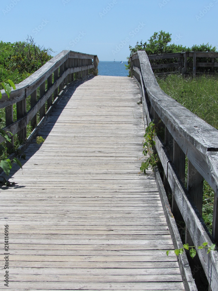 A wooden walkway leading over a hill to the ocean and beach A wooden walkway leading over a hill to the ocean and beach