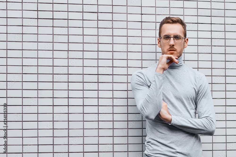 Hipster wearing glasses, standing near the wall made of small tiles Hipster wearing glasses, standing near the wall made of small tiles