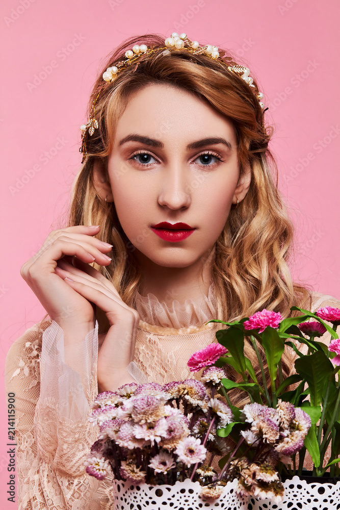 Fashion photo of young woman on pink background wearing gold diadem with flowers near her face