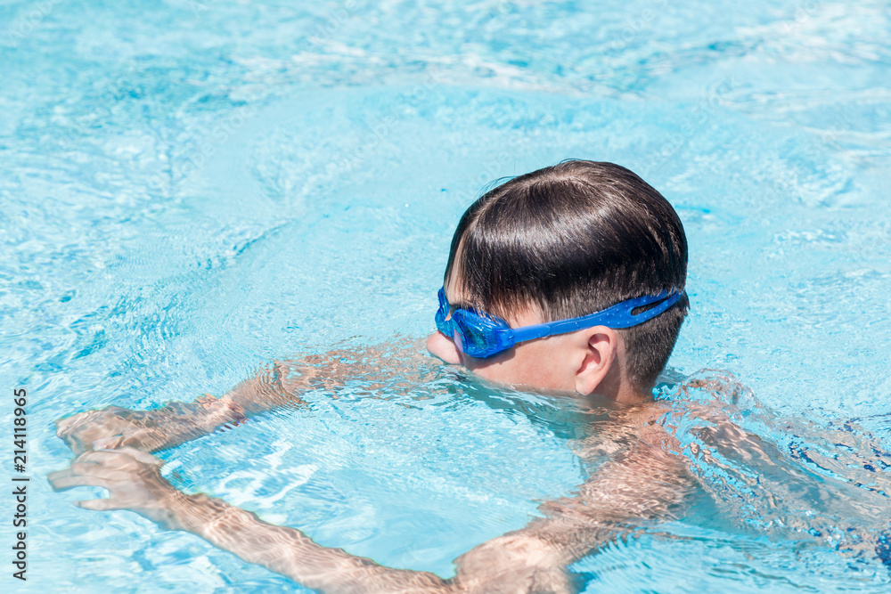 Close-up portrait of teenage boy in goggles in swimming pool.