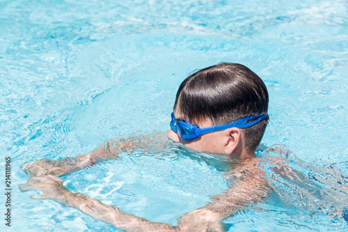 Close-up portrait of teenage boy in goggles in swimming pool.