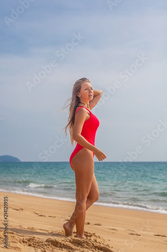 Sexy woman in red swimsuit stands on the beach near ocean, Phuket, Thailand