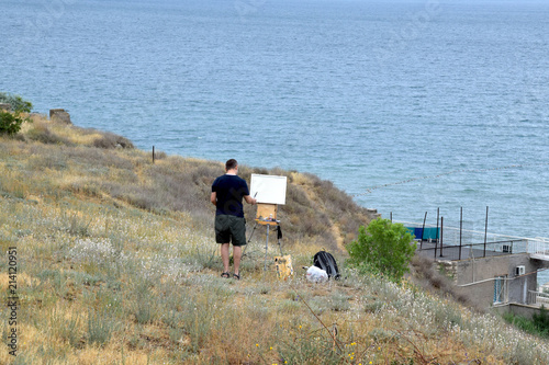 художник рисует море на высоком берегу